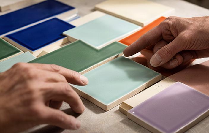 Mani che confrontano campioni di piastrelle smaltate su un tavolo dell'atelier ceramico